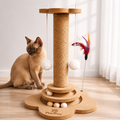 Kitten playing with a wooden cat toy with feathers and balls on a light wood floor.
